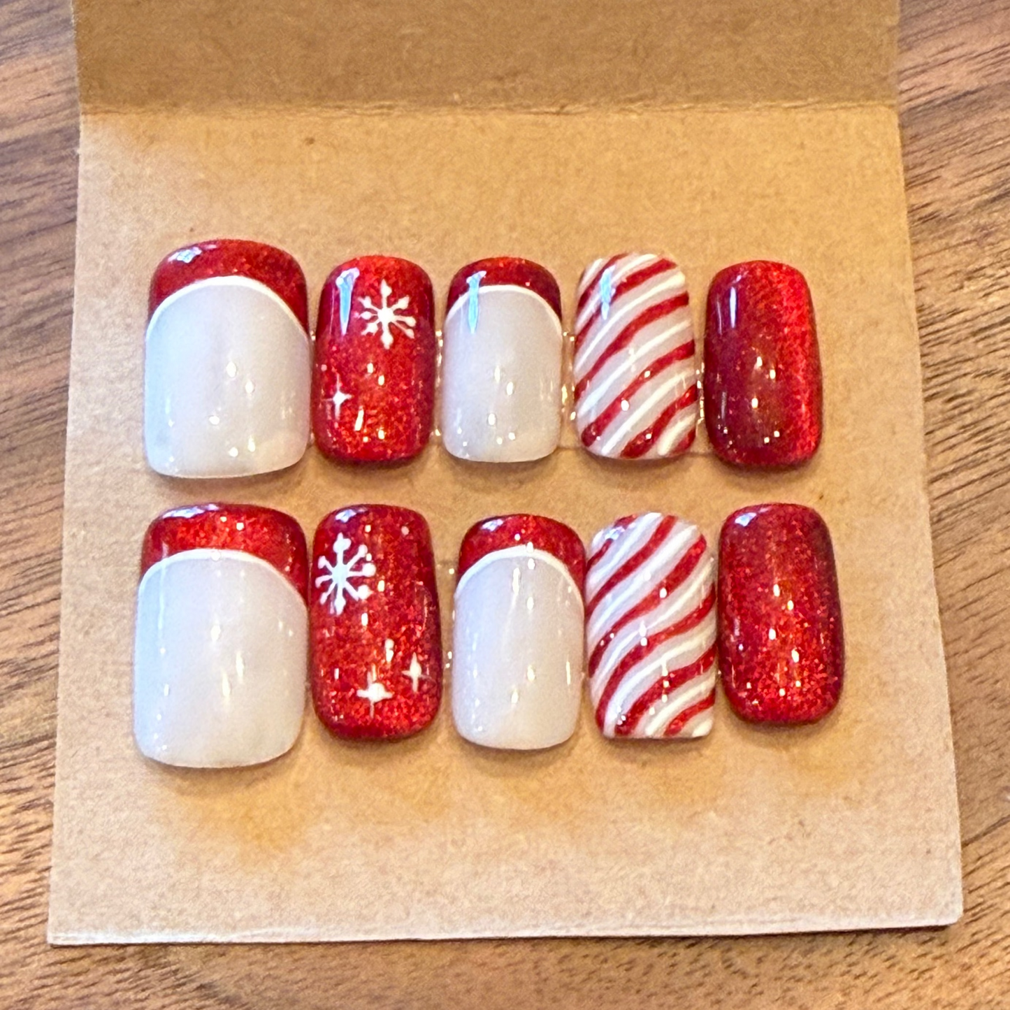 Set of red, white, and candy cane patterned nails on a brown paper background