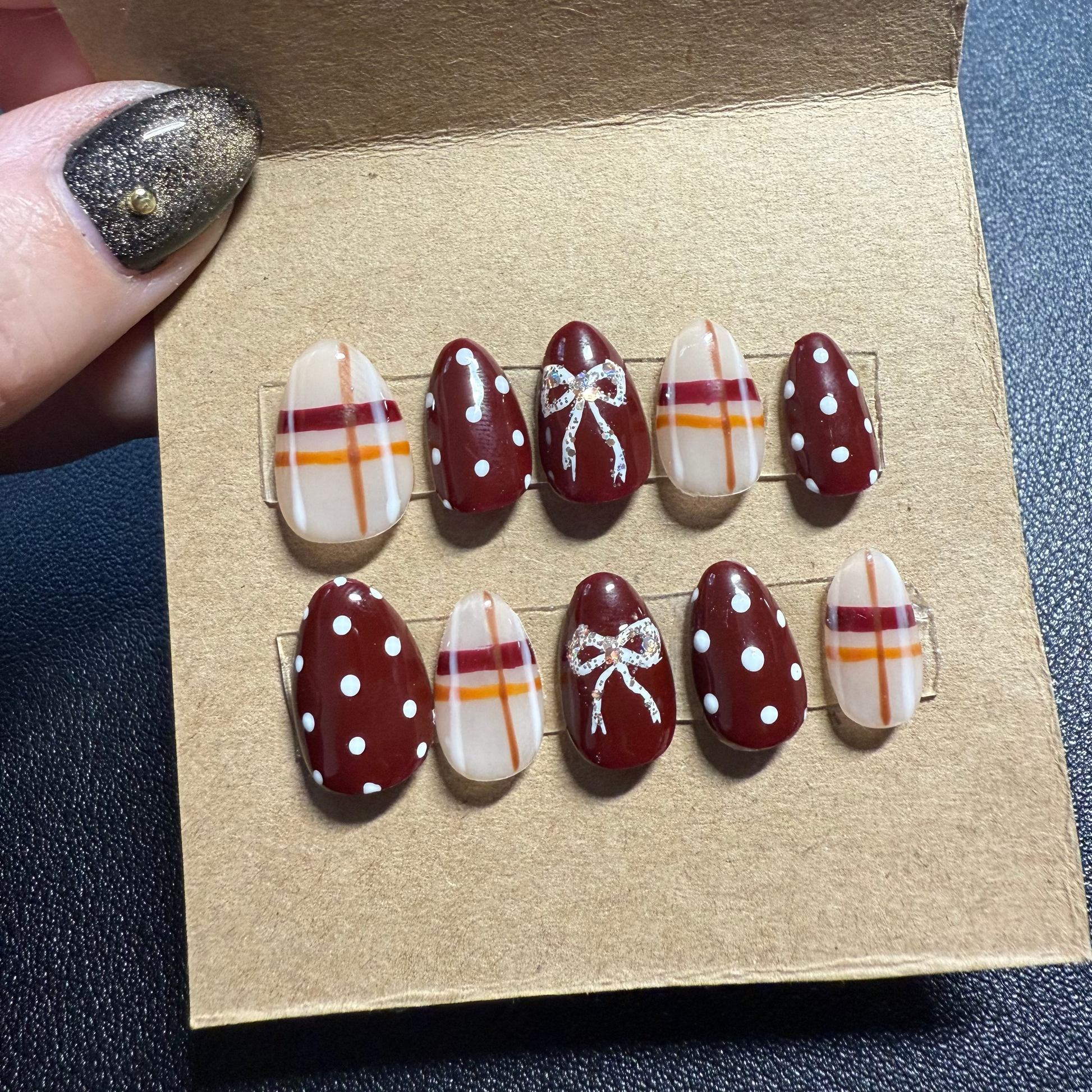 Set of decorative press on nails in burgundy and gold on a cardboard backing
