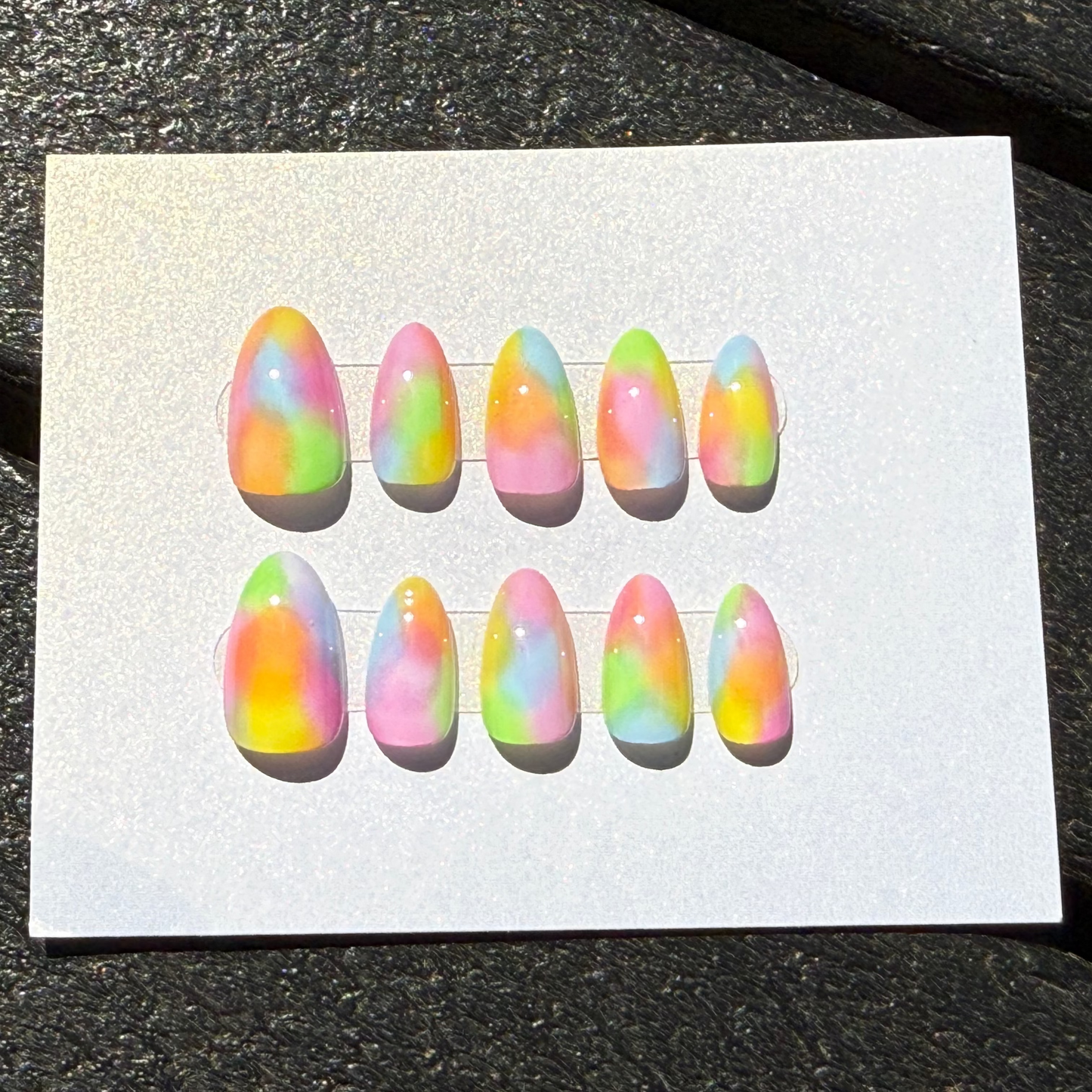 Set of colorful press on nails on a white card against a dark background