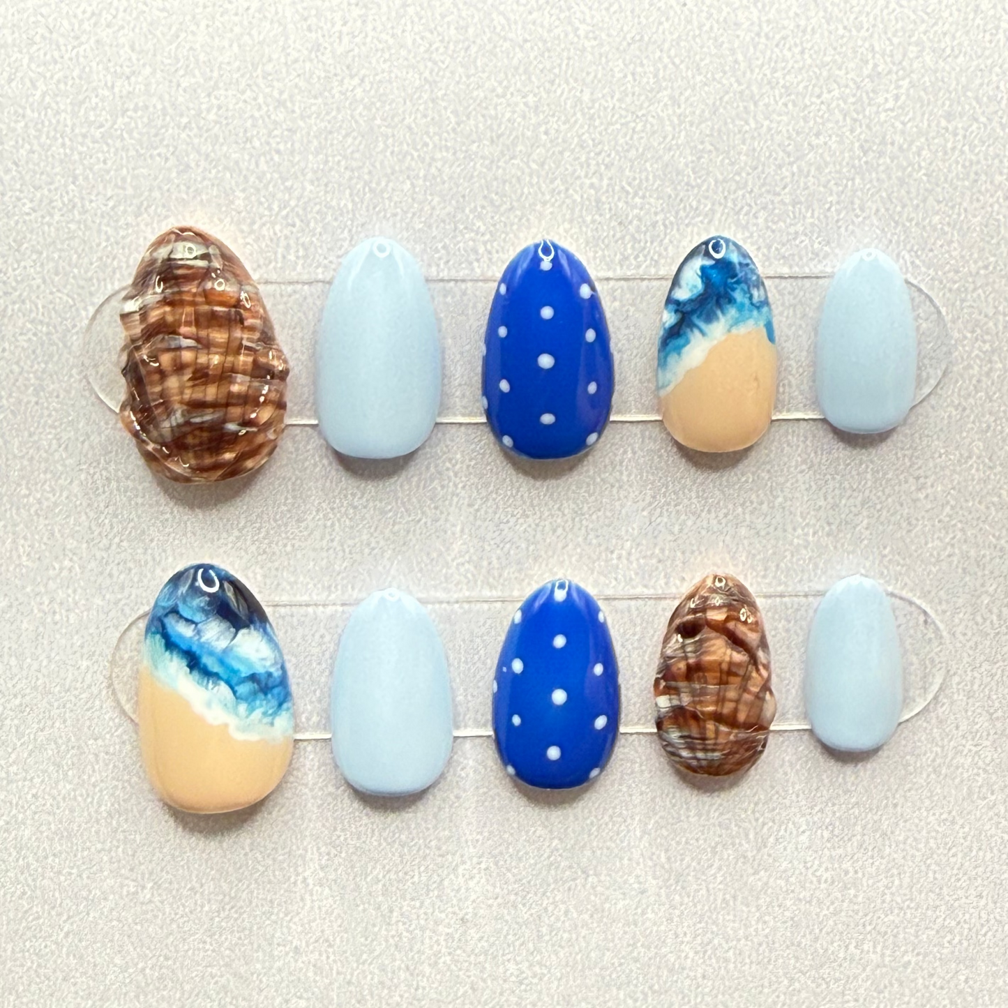 Set of decorative press on nails with blue polka dots, wave and shell designs on a neutral background
